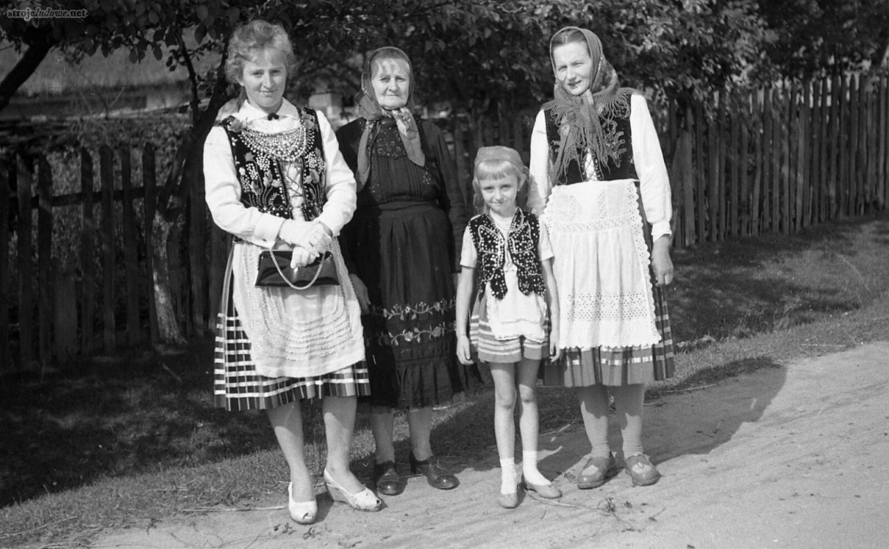 Trzy pokolenia kobiet w strojach z okolic Piotrkowa, 1953 r., Archiwum Etnograficzne Muzeum Archeologicznego i Etnograficznego w Łodzi, fot. K. Wecel

Najstarsza z kobiet w tradycyjnym stroju z kaftanem i długim czarnym haftowanym fartuchu, młodsze w gorsetach. Matka z dzieckiem jeszcze w gorsecie haftowanym koralikami na przodach w tzw. rózgi, białym fartuchu z wstawkami z fabrycznej koronki i chustce na głowie;  druga z kobiet, młodsza, w gorsecie z rozbudowanym haftem, „dmuchanych” koralach według mody krakowskiej i małym fartuszku z naszyciami karbowanymi ze wstążek. Moda krakowska w tym regionie rozpowszechniła się już w okresie międzywojennym. Dziewczynka w gorsecie i spódniczce jednokolorowej tzw. kretance z naszytymi wstążkami, ubrana jest według najmłodszej „mody krakowskiej”. 
