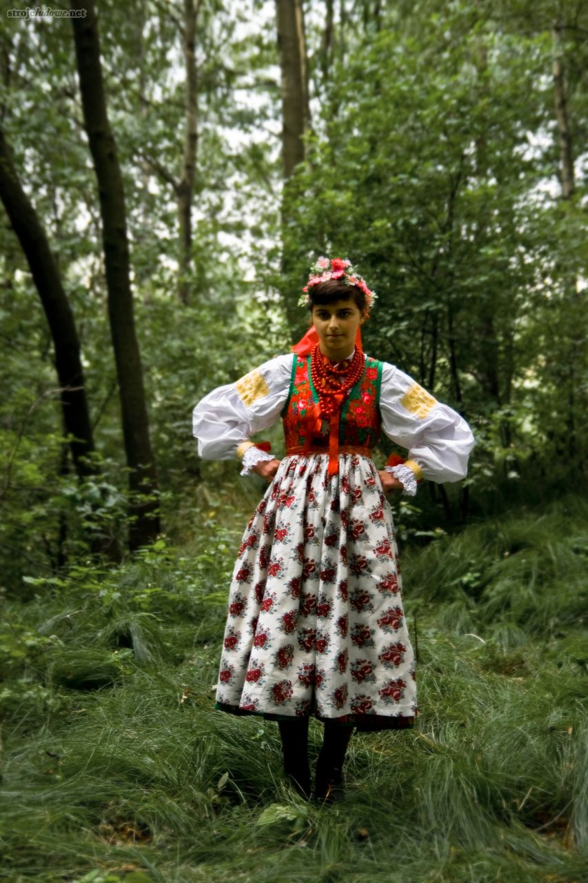 Dziewczyna w przedwojennym stroju na pierwszą niedzielę miesiąca, charakterystyczny na tę okazję fartuch „z dużą  różą” [Püśkjyś]. 2008 r., fot. Wojciech Romański

Odświętny strój panny składał się z białej koszuli (<em>jypła</em>), zdobionej na przyramkach i nadgarstkach haftami, spiętej pod szyją kwiecistą wstążką. Tło wstążki, w zależności od okazji, było białe lub czerwone. Na koszuli leżał oplecek (<em>gyśtałt</em>), zszyty ze spódnicą (<em>rök</em>) . Przeważnie był on brokatowy i żakardowy, <em>lecz zdarzały się również szyte z materiału tybetowego, które mieszkańcy sprowadzali z Krakowa (dlatego</em> tybetowe oplecki nazywane są krakowskimi).