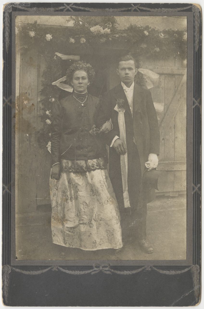 Nowożeńcy, panna młoda w stroju pszczyńskim, z wiankiem z mirtu (śl. merty) na głowie, na jej szyi ozdobny łańcuszek, na którym zawieszony jest medalik w kształcie serca, miejscowość niezidentyfikowana, lata 1920-1930, autor nieznany, z kolekcji Muzeum Śląskiego w Katowicach.