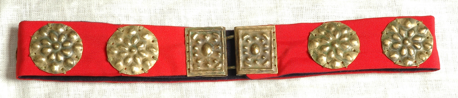 Pas, ze zbiorów Muzeum w Koszalinie , fot. J. Święch
Pas tworzyły dwie warstwy tkaniny (spodnia z sukna granatowego lub czarnego, wierzchnia z czerwonego<strong><em> </em></strong>jedwabiu lub sukna). Na takim podkładzie mocowano dziesięć okrągłych plakietek o średnicy około 5 cm. Zapięcie pasa (tak jak i aksamitki) tworzyła dwuczęściowa klamra wykonana, podobnie jak zdobiące pas plakietki, z blachy mosiężnej lub srebrnej.